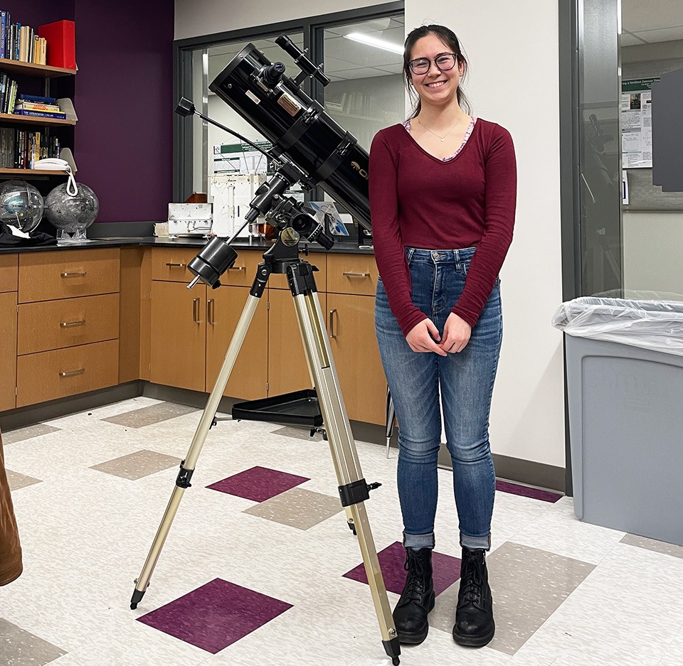 Rosie Friend stands by a telescope in the astronomy lab