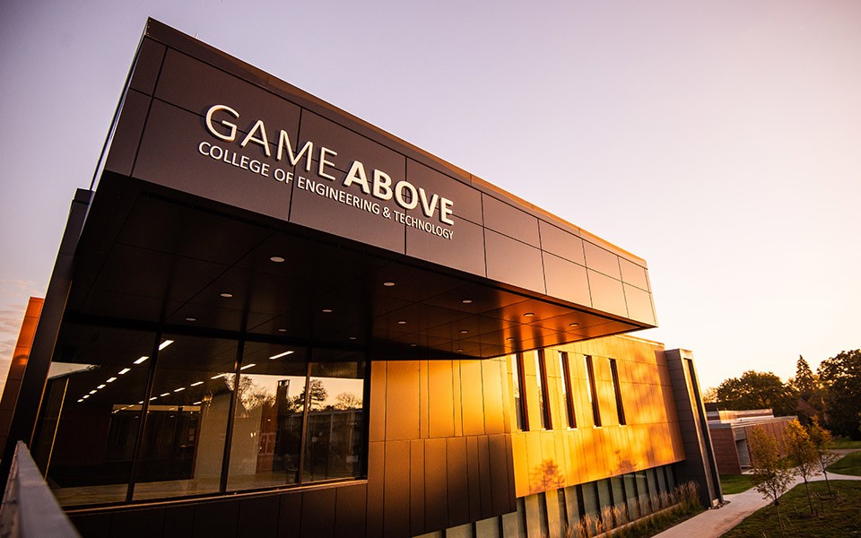The exterior of Sill Hall/GameAbove College of Engineering & Technology sign is lit  by the evening sun.