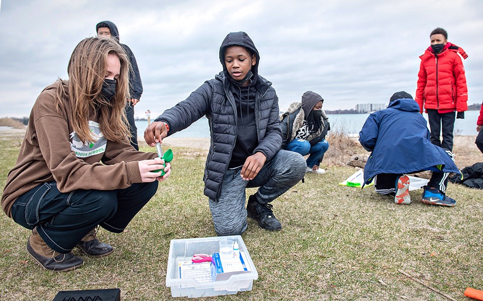 A group of students testing water on Belle Isle in Detroit on a cloudy spring day.