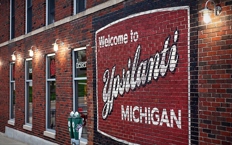 Lighted by outdoor lamps, a sign painted on a brick wall of a downtown business says, "Welcome to Ypsilanti, Michigan."