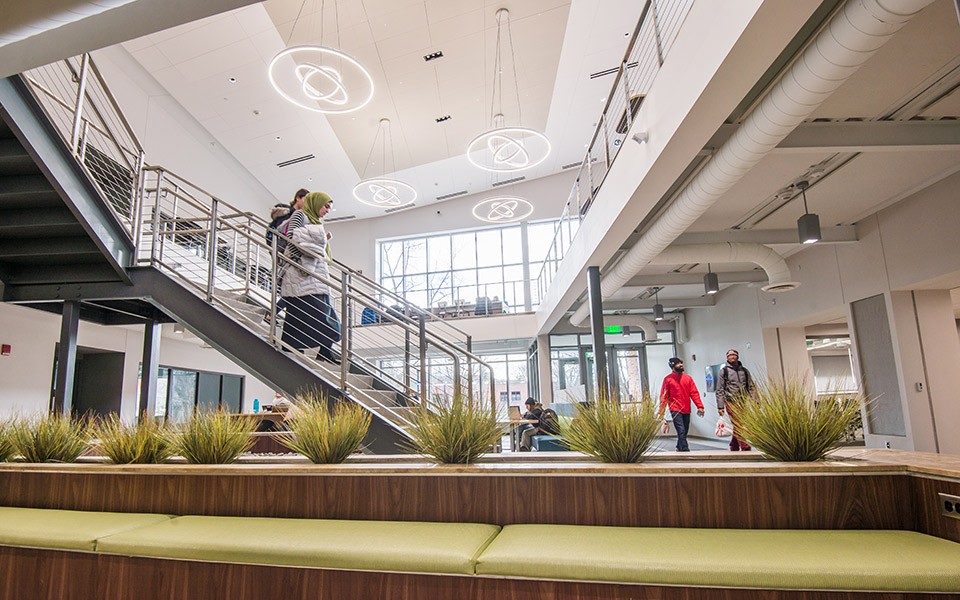 Students walk through the atrium of the renovated Strong Hall with plants in the foreground of the open space.