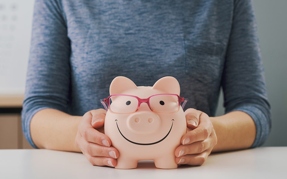 A person's hands hold a piggy bank that has a smile and a pair of glasses on it.