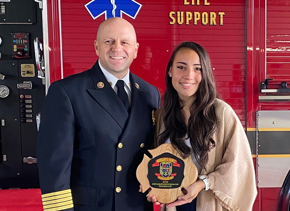 Margarita Howes holds a Civilian Lifesaving Award plaque which she received for saving a drowning man's life with CPR. Next to her is Ann Arbor fire chief, Mike Kennedy.