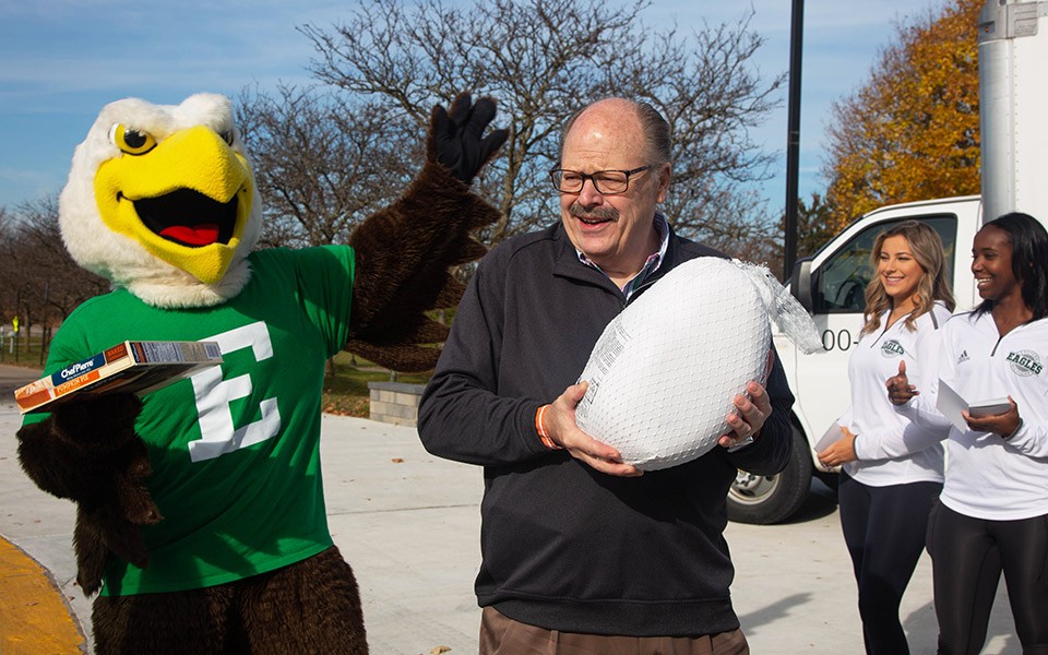 Swoop waves while President Smith holds a frozen turkey to be given out at the Thankful for You drive-thru event.
