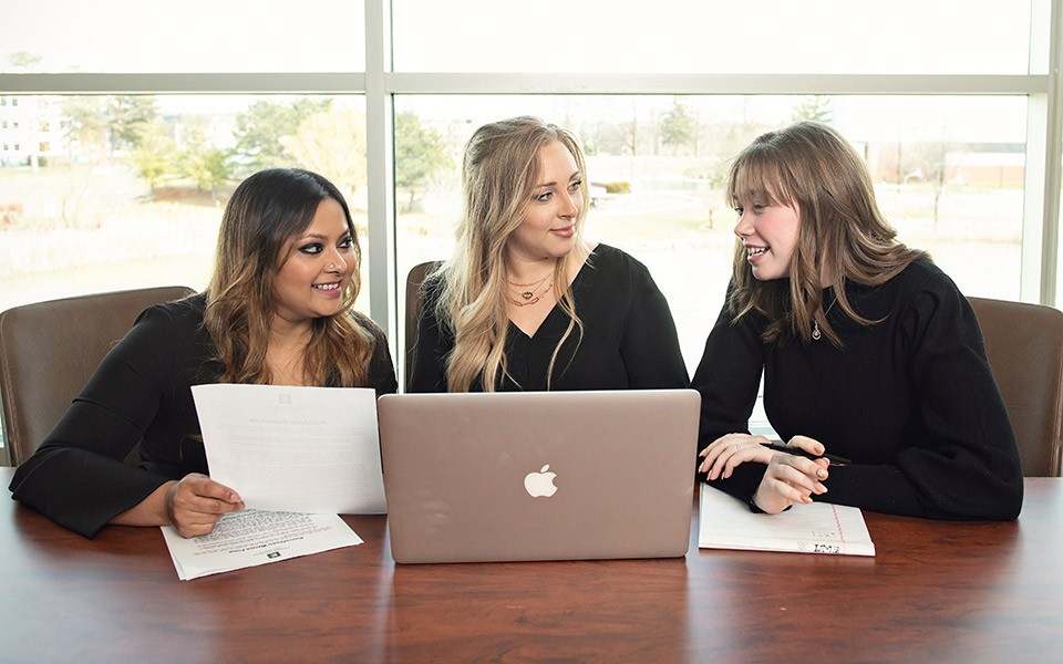 Three business grad students are consulting around a laptop.
