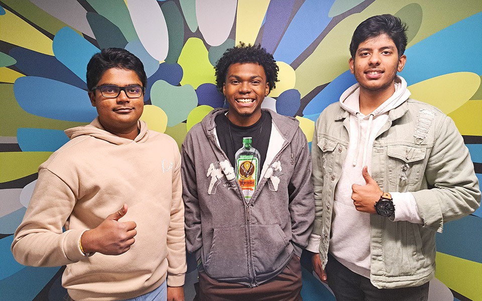 Chanuth Jayatissa, Cameron Jones, and Karthikeya Thota of the BlackHatHackers in front of a mural wall with thumbs up.