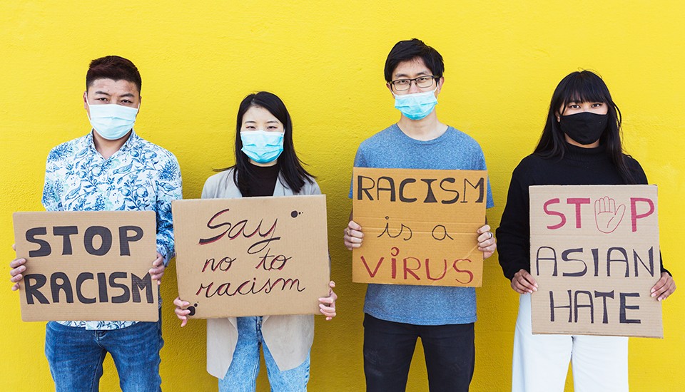 Young Asian people wearing face masks holding signs protesting against racism.