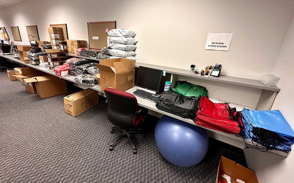 A long desk is piled with supplies and bags to be filled with supplies.