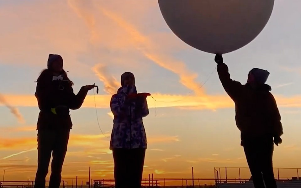 Silhouettes of students releasing a weather balloon into the air.
