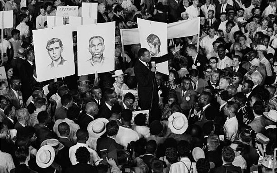 Historical photo of MLK at a civil rights event with signs featuring the slain activists