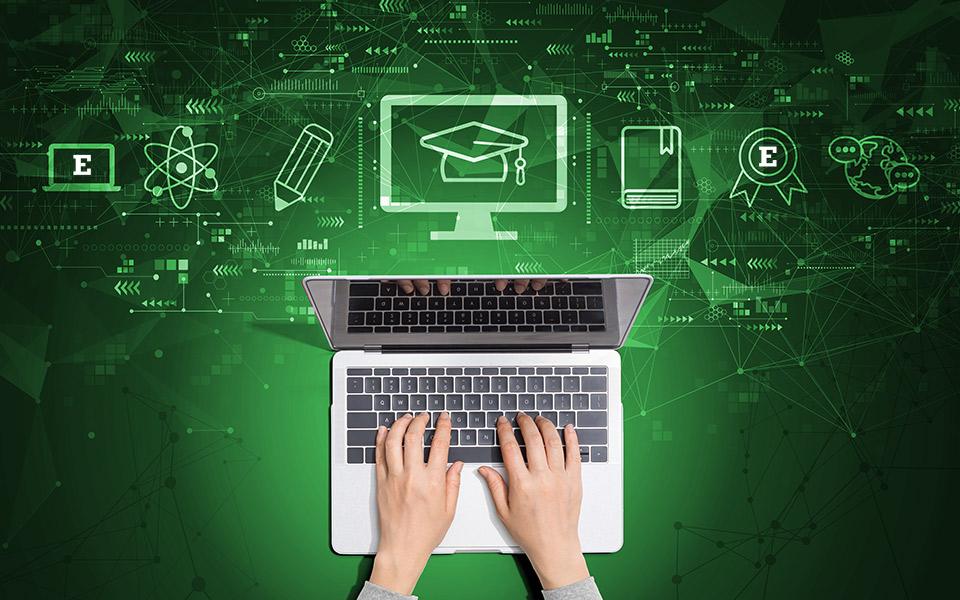 overhead view of hands on a laptop with graphic icon of a grad cap and other college symbols