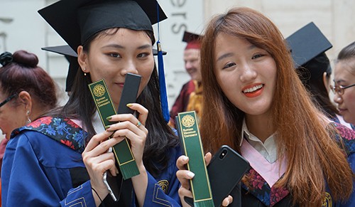 Graduating students in China hold up EMU bookmarks.