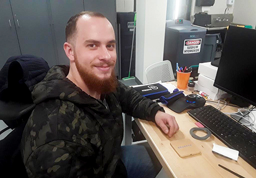 Lukas Brockway sits at a computer wearing a camouflage hoodie